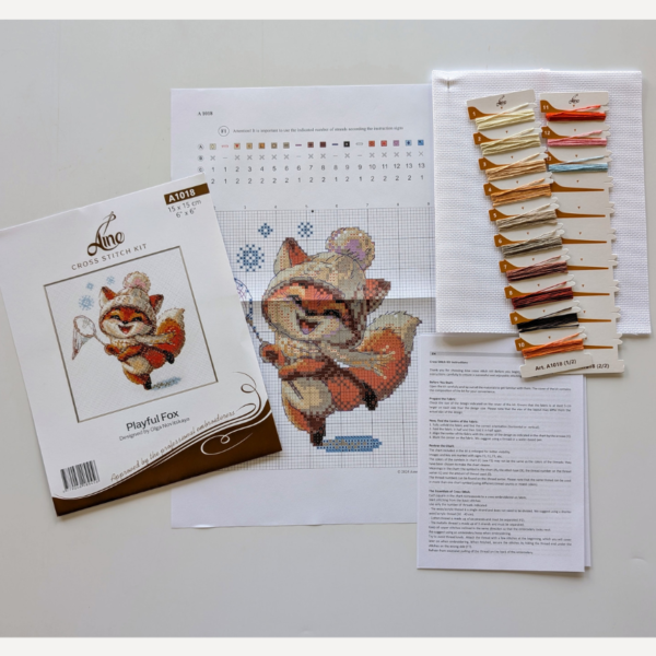 Playful Fox cross-stitch kit showing a fox in hat and scarf catching snowflakes in winter, embroidery design by Aine.