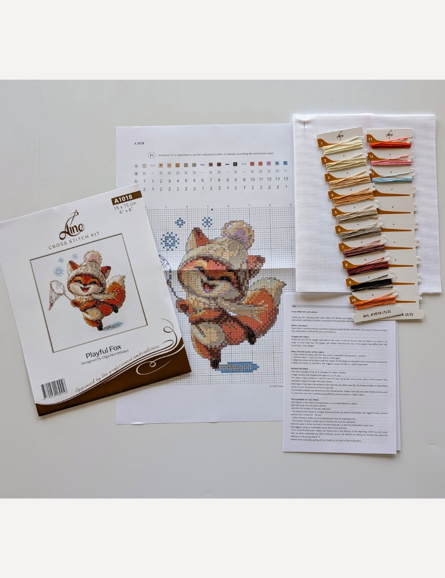 Playful Fox cross-stitch kit showing a fox in hat and scarf catching snowflakes in winter, embroidery design by Aine.