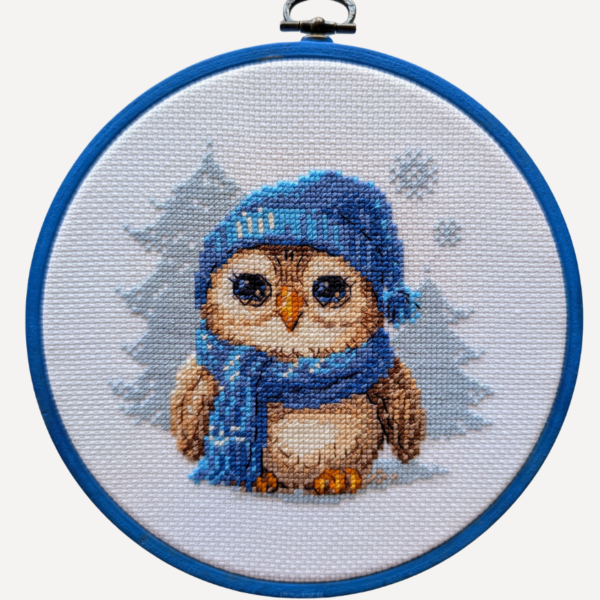 Cuddly Owl cross-stitch kit showing an owl in blue hat and scarf standing in snow, winter embroidery design by Aine.