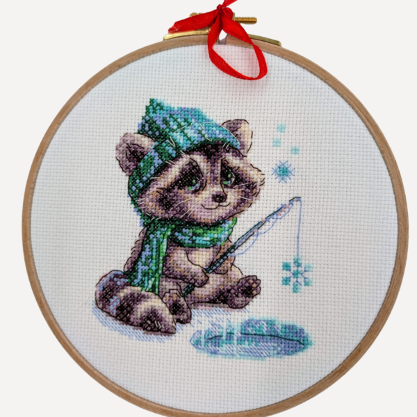 Aine A1017 Curious Raccoon Cross Stitch Kit – counted cross stitch design featuring a raccoon in a green scarf and hat, sitting beside a frozen pond, fishing for snowflakes; includes 14 ct white Zweigart Aida fabric, 15 Anchor stranded cotton threads, needle, color chart, and instructions; finished size 15 x 15 cm (6 x 6 inches).