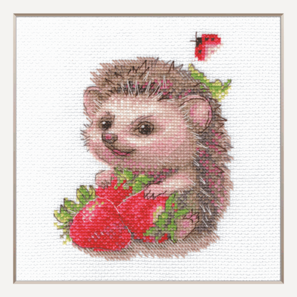 A completed cross-stitch of a smiling hedgehog holding two bright red strawberries, with a small ladybug above, stitched in warm browns, pinks, and reds on white Aida fabric.