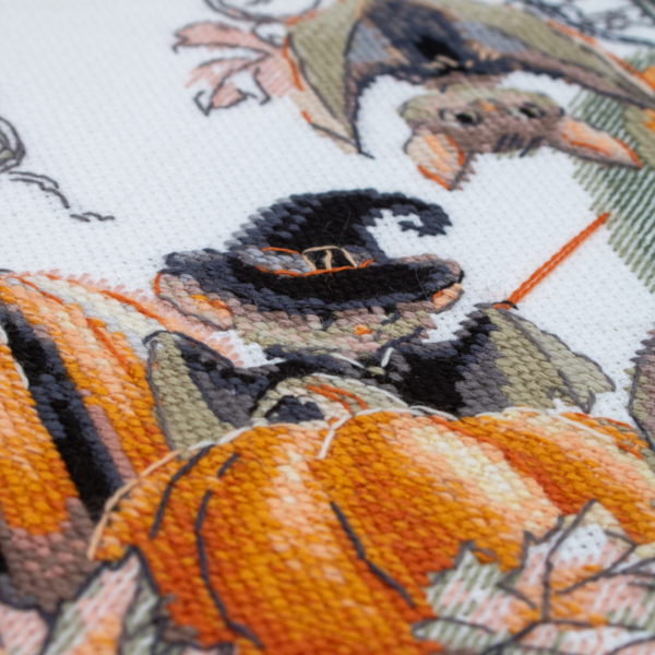 A completed cross-stitch of bats and pumpkins in a Halloween theme, with striped and checkered pumpkins, autumn leaves, and a bat in a witch hat holding a wand.