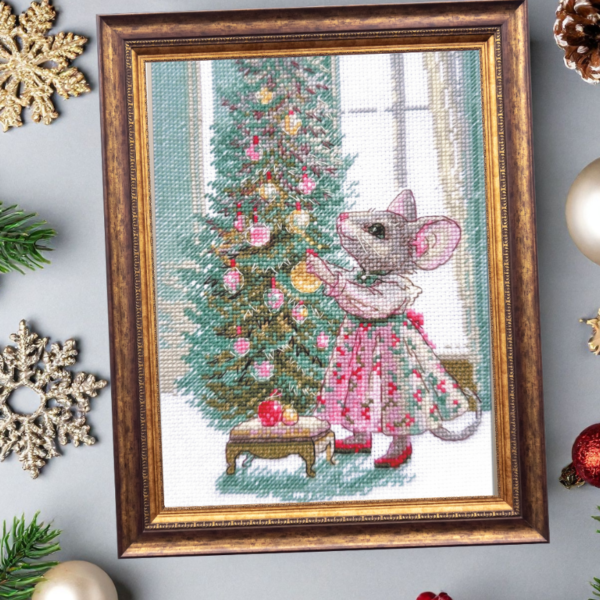 A completed cross-stitch of a mouse in a festive dress decorating a Christmas tree with ornaments, stitched in warm reds, greens, and golds on white Aida fabric.