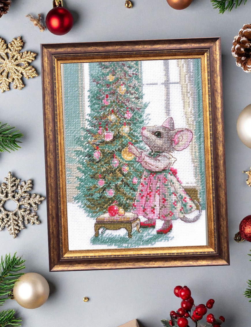 A completed cross-stitch of a mouse in a festive dress decorating a Christmas tree with ornaments, stitched in warm reds, greens, and golds on white Aida fabric.