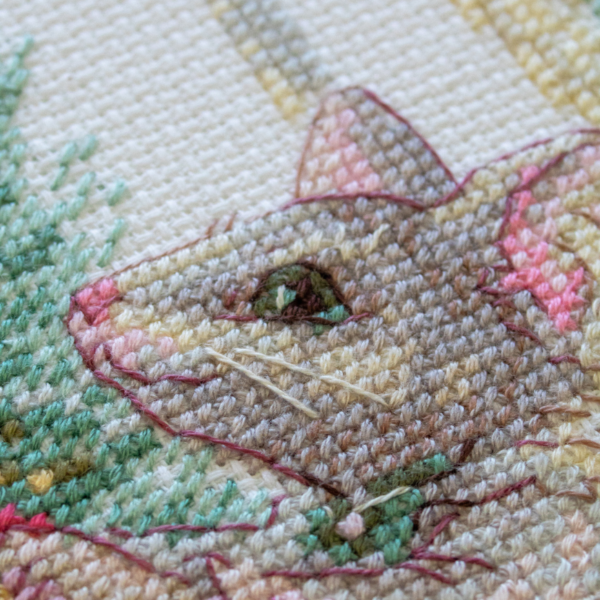 A completed cross-stitch of a mouse in a festive dress decorating a Christmas tree with ornaments, stitched in warm reds, greens, and golds on white Aida fabric.