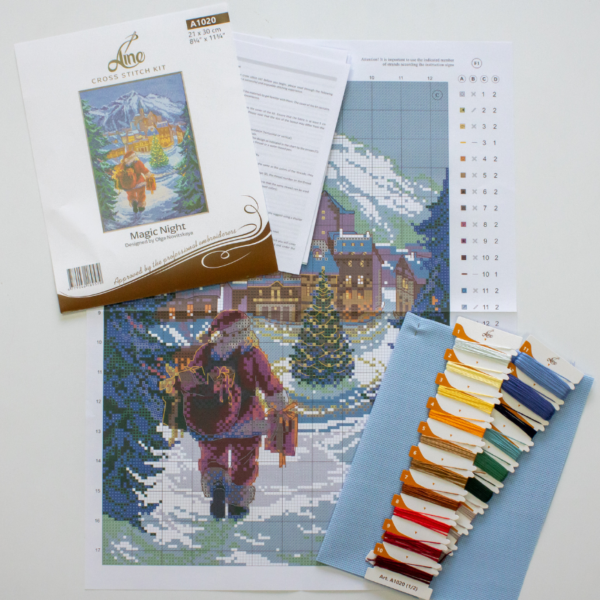 A completed cross-stitch of Santa Claus walking through a snowy village square with a glowing Christmas tree, surrounded by decorated houses and snowy mountains in the background.