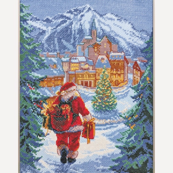 A completed cross-stitch of Santa Claus walking through a snowy village square with a glowing Christmas tree, surrounded by decorated houses and snowy mountains in the background.