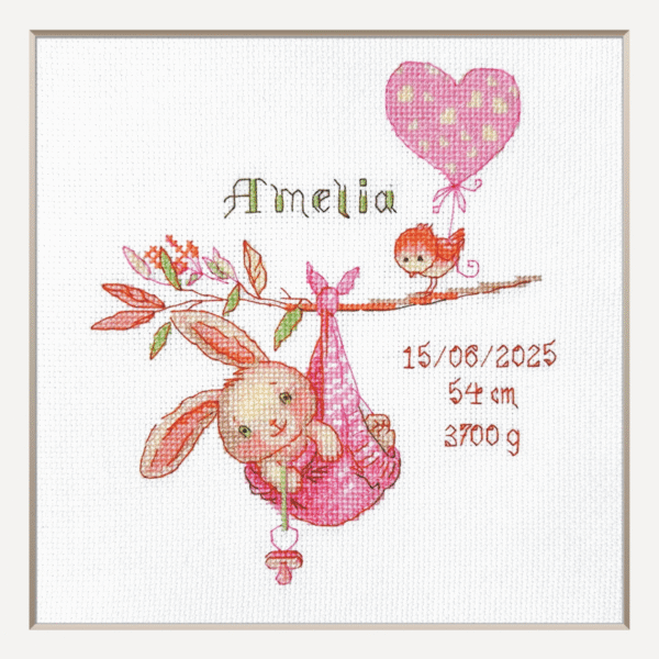 A completed cross-stitch birth sampler featuring a bunny in a pink sling hanging from a branch, with a bird holding a pink heart balloon and space for baby details.