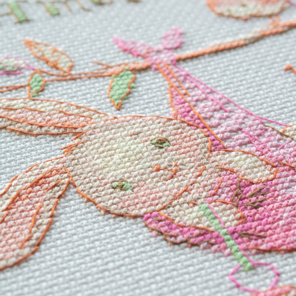 A completed cross-stitch birth sampler featuring a bunny in a pink sling hanging from a branch, with a bird holding a pink heart balloon and space for baby details.