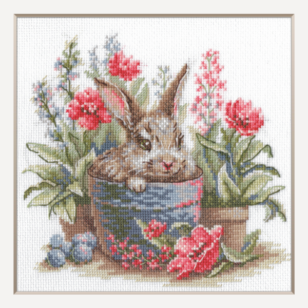 A completed cross-stitch of a brown bunny peeking out of a blue flower pot surrounded by red flowers and green plants in a garden scene.