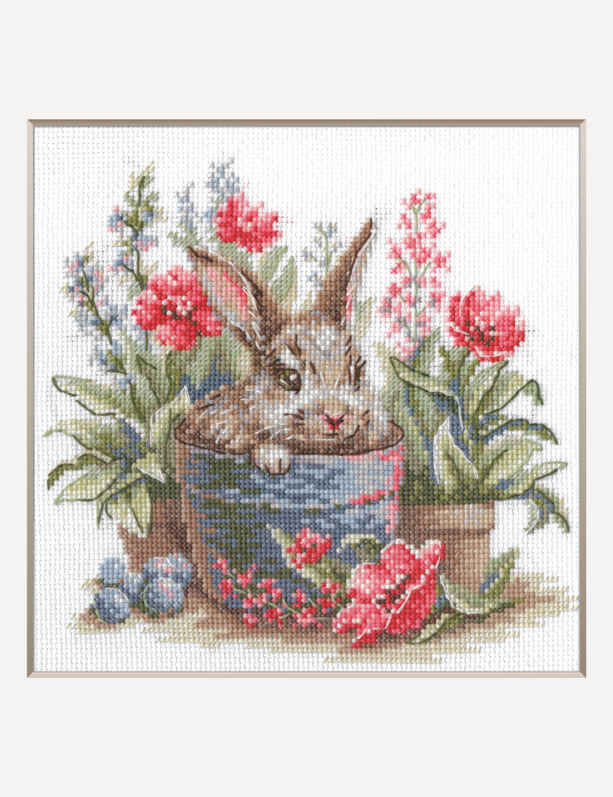 A completed cross-stitch of a brown bunny peeking out of a blue flower pot surrounded by red flowers and green plants in a garden scene.