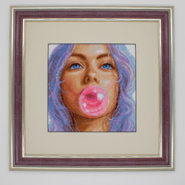 A completed cross-stitch of a girl with pastel purple hair blowing a pink bubblegum bubble, with bright blue eyes and soft blended tones.
