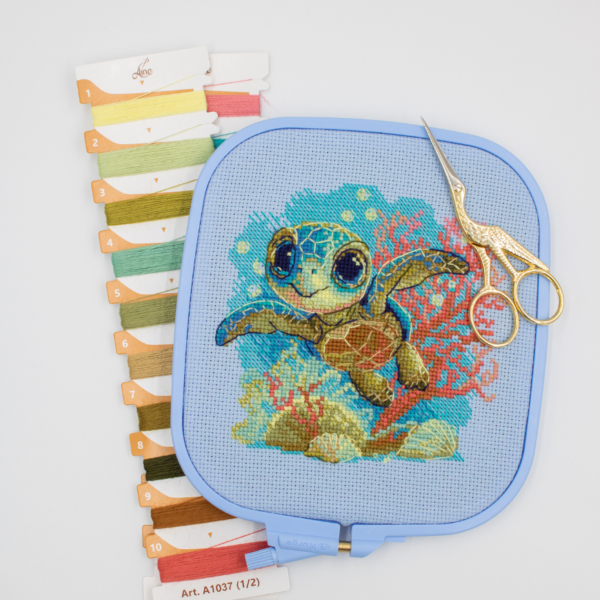 Cross-stitch kit showing a baby sea turtle underwater with coral, seashells, and a blue ocean background.