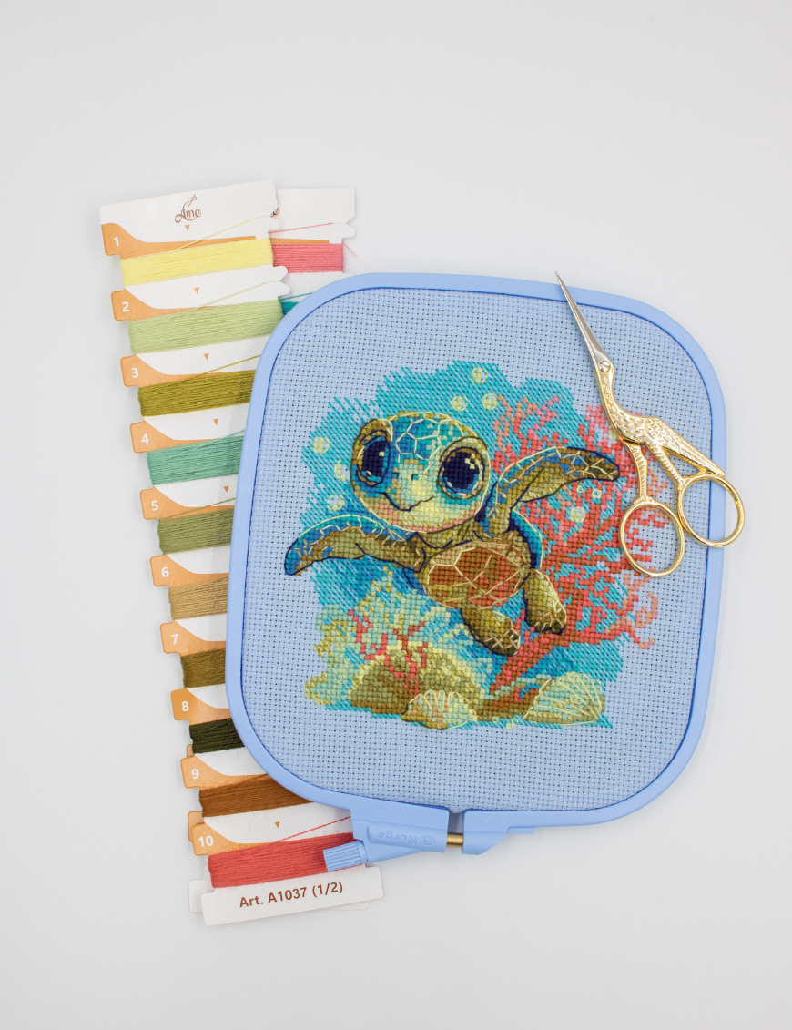 Cross-stitch kit showing a baby sea turtle underwater with coral, seashells, and a blue ocean background.