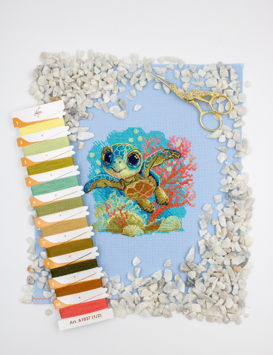 Cross-stitch kit showing a baby sea turtle underwater with coral, seashells, and a blue ocean background.