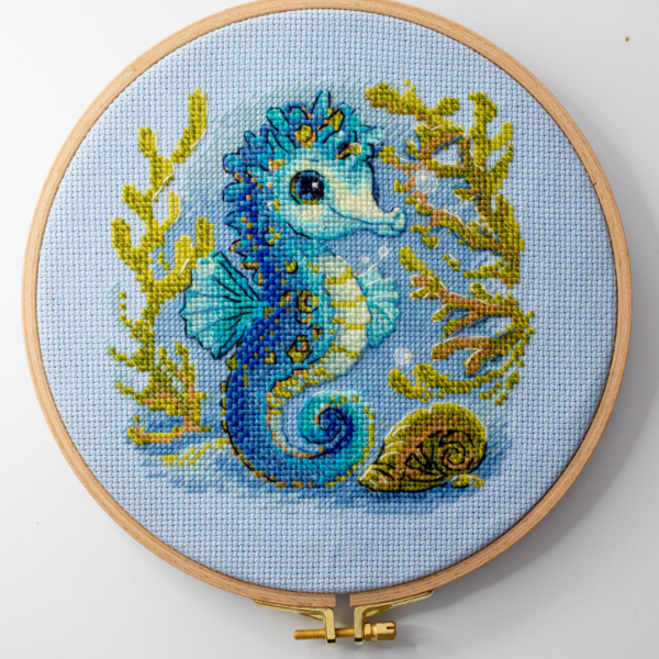 Baby Sea Horse cross stitch kit showing a blue baby seahorse underwater with golden seaweed and a shell.