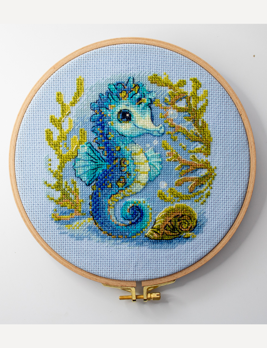 Baby Sea Horse cross stitch kit showing a blue baby seahorse underwater with golden seaweed and a shell.
