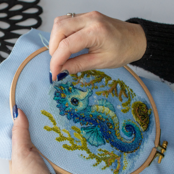 Baby Sea Horse cross stitch kit showing a blue baby seahorse underwater with golden seaweed and a shell.