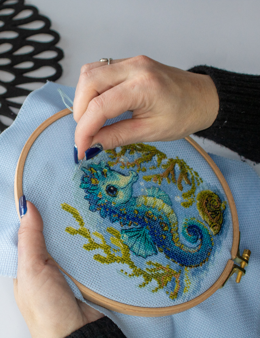 Baby Sea Horse cross stitch kit showing a blue baby seahorse underwater with golden seaweed and a shell.