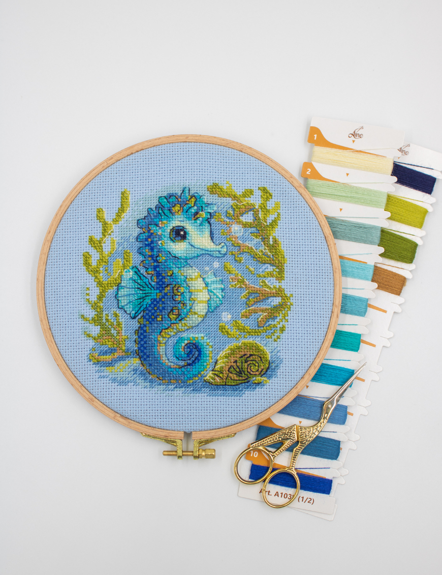 Baby Sea Horse cross stitch kit showing a blue baby seahorse underwater with golden seaweed and a shell.