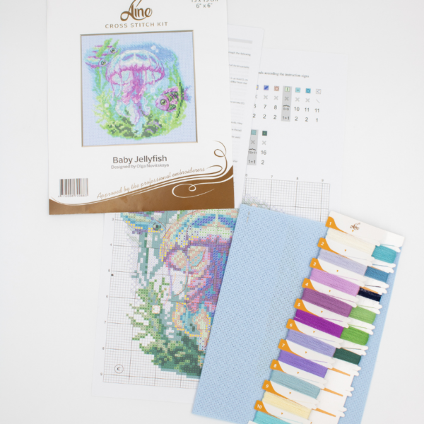 Baby Jellyfish cross stitch kit showing a pink and purple jellyfish underwater with green sea plants, bubbles, and three fish.