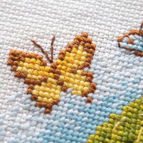 A1042 Blossom Gnome Aine Cross-Stitch Kit featuring a garden gnome in a green hat surrounded by pink flowers, foliage, and butterflies.