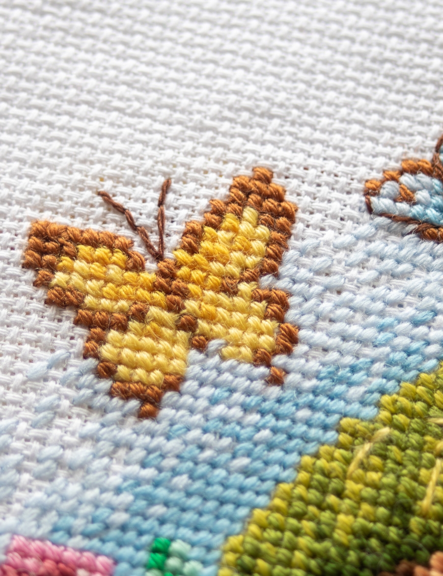 A1042 Blossom Gnome Aine Cross-Stitch Kit featuring a garden gnome in a green hat surrounded by pink flowers, foliage, and butterflies.