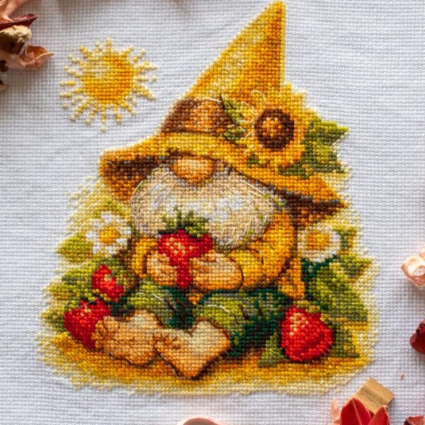 A1043 Sunshine Gnome Aine Cross-Stitch Kit featuring a garden gnome in a yellow sunflower hat surrounded by red flowers, daisies, and green foliage.