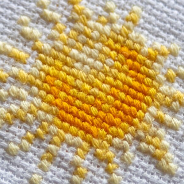 A1043 Sunshine Gnome Aine Cross-Stitch Kit featuring a garden gnome in a yellow sunflower hat surrounded by red flowers, daisies, and green foliage.