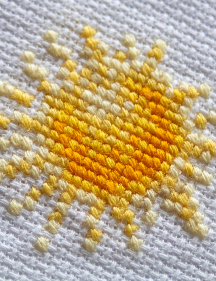 A1043 Sunshine Gnome Aine Cross-Stitch Kit featuring a garden gnome in a yellow sunflower hat surrounded by red flowers, daisies, and green foliage.