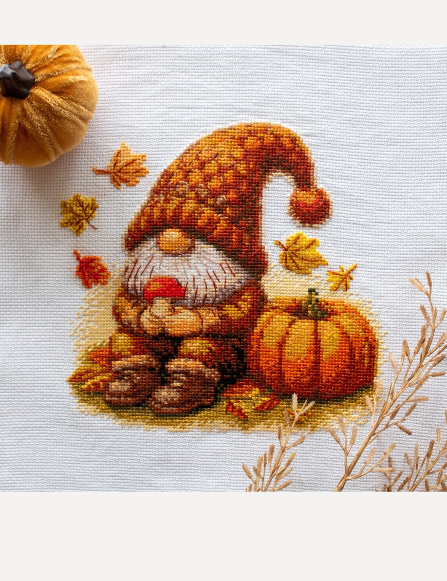 A1044 Harvest Gnome Aine Cross-Stitch Kit featuring an autumn gnome with a large orange pumpkin, colorful fall leaves, and a tiny red mushroom.