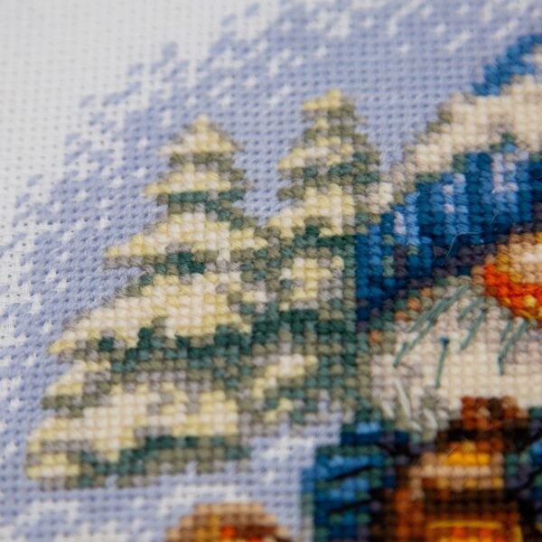 A1045 Snowy Gnome Aine Cross-Stitch Kit featuring a winter gnome with a blue snowy hat, glowing lantern, wooden sled, bird, and snow-covered evergreen trees.