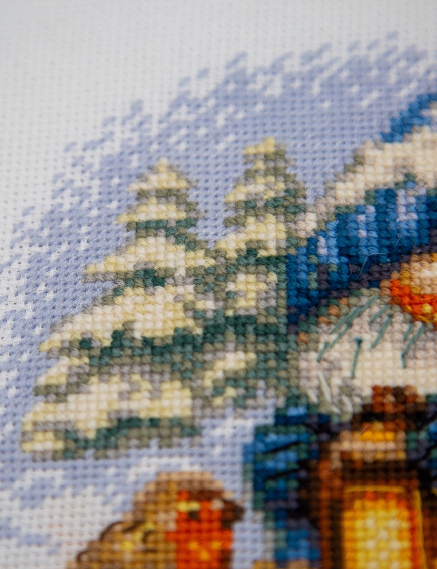 A1045 Snowy Gnome Aine Cross-Stitch Kit featuring a winter gnome with a blue snowy hat, glowing lantern, wooden sled, bird, and snow-covered evergreen trees.
