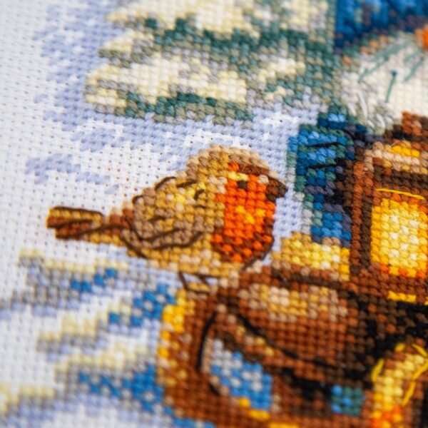 A1045 Snowy Gnome Aine Cross-Stitch Kit featuring a winter gnome with a blue snowy hat, glowing lantern, wooden sled, bird, and snow-covered evergreen trees.