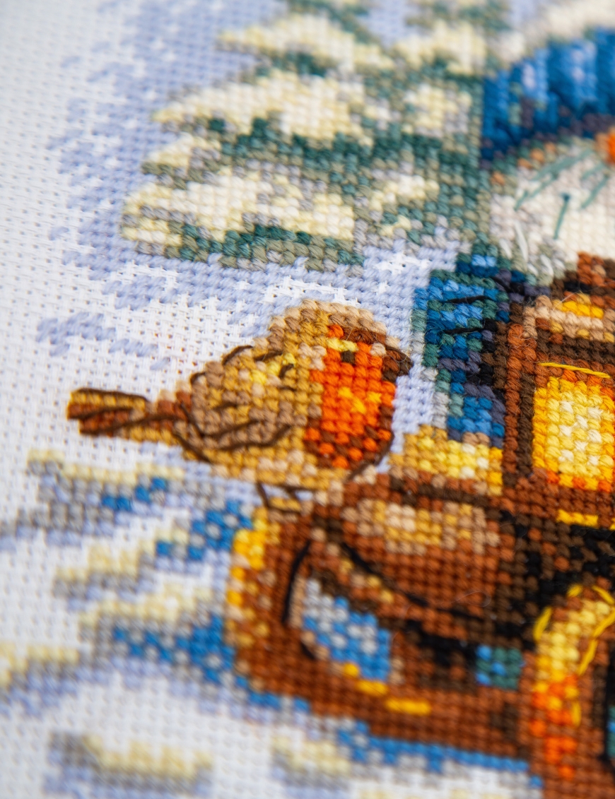 A1045 Snowy Gnome Aine Cross-Stitch Kit featuring a winter gnome with a blue snowy hat, glowing lantern, wooden sled, bird, and snow-covered evergreen trees.