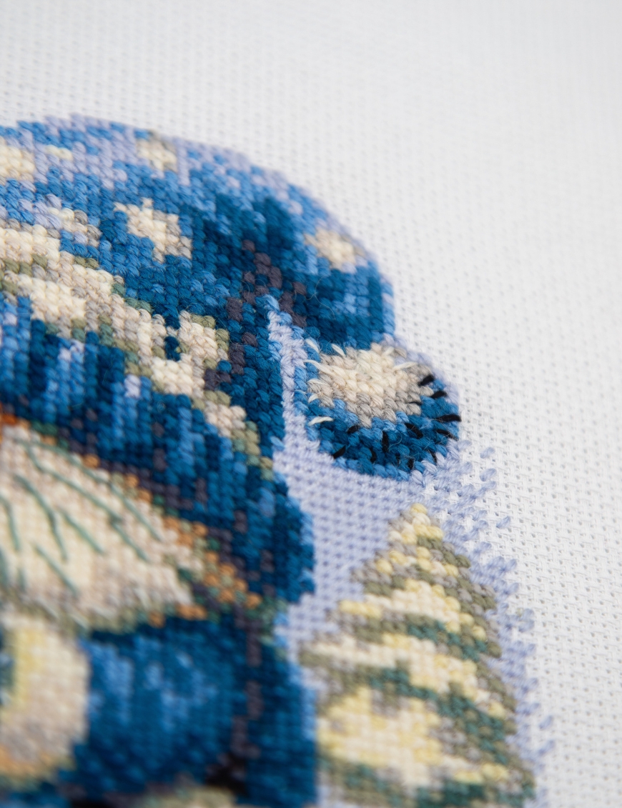 A1045 Snowy Gnome Aine Cross-Stitch Kit featuring a winter gnome with a blue snowy hat, glowing lantern, wooden sled, bird, and snow-covered evergreen trees.