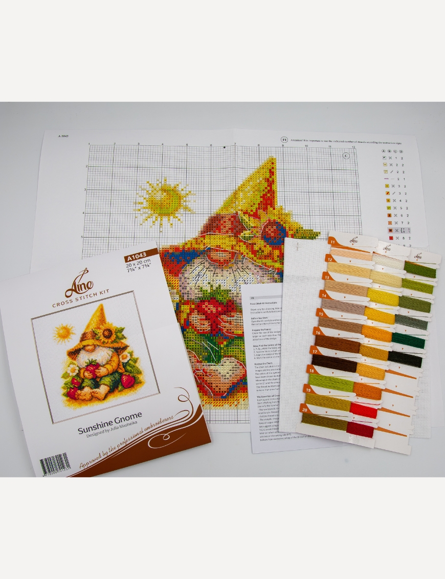 A1043 Sunshine Gnome Aine Cross-Stitch Kit featuring a garden gnome in a yellow sunflower hat surrounded by red flowers, daisies, and green foliage.