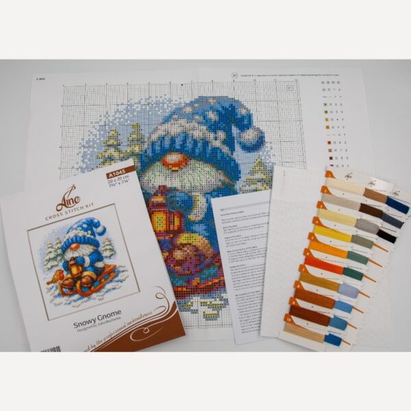 A1045 Snowy Gnome Aine Cross-Stitch Kit featuring a winter gnome with a blue snowy hat, glowing lantern, wooden sled, bird, and snow-covered evergreen trees.