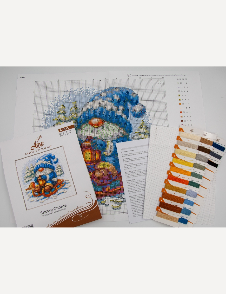 A1045 Snowy Gnome Aine Cross-Stitch Kit featuring a winter gnome with a blue snowy hat, glowing lantern, wooden sled, bird, and snow-covered evergreen trees.