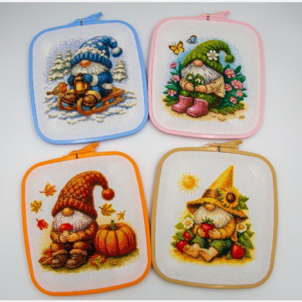 Four seasonal Aine gnome cross-stitch designs displayed in colorful square embroidery hoops, featuring Blossom, Sunshine, Harvest, and Snowy Gnomes.