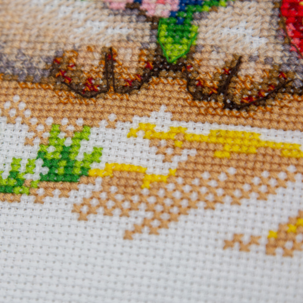 A completed cross-stitch picture of three baby goats on a beach: one wearing blue sunglasses beside a pink flower, one wearing a yellow snorkel mask and tube inside a red inflatable swim ring with yellow stars, and one drinking a tropical cocktail with a paper umbrella, set against a blue sky with white clouds.