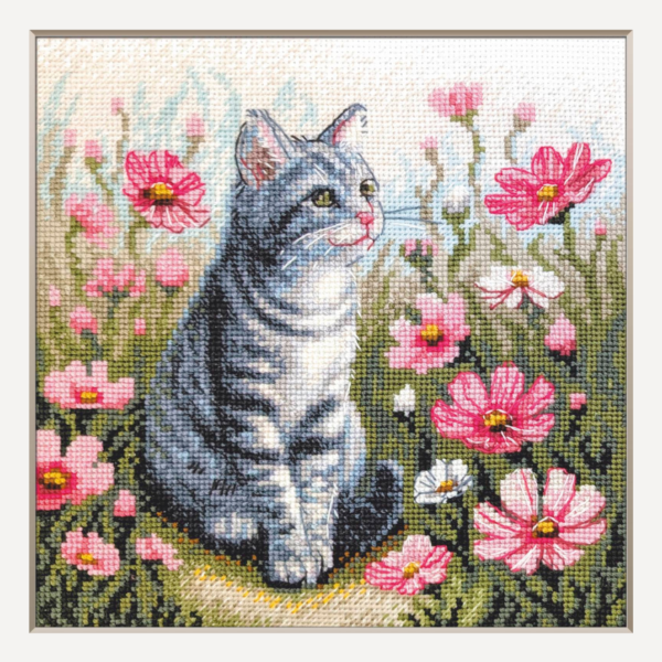 A completed cross-stitch portrait of a grey tabby cat with white markings and green eyes, sitting among tall pink cosmos flowers and a few white blooms, with green foliage and a pale blue sky in the background.