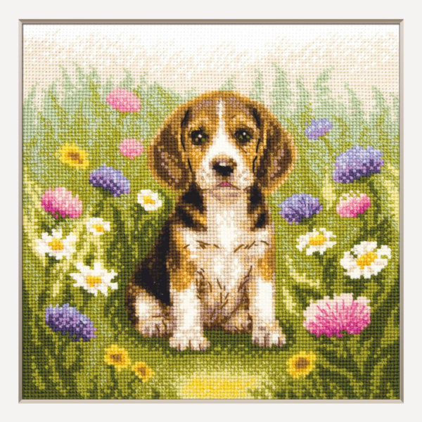 A completed cross-stitch portrait of a tricolor beagle puppy with long floppy ears sitting in a green meadow, surrounded by pink and purple wildflowers, white daisies and yellow blooms.