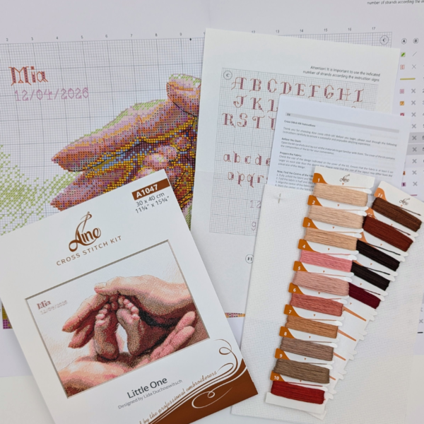 The A1047 Little One cross-stitch kit box laid out with the colour chart, an alphabet chart, the instruction sheet, pre-sorted threads on numbered cards and white Aida fabric.