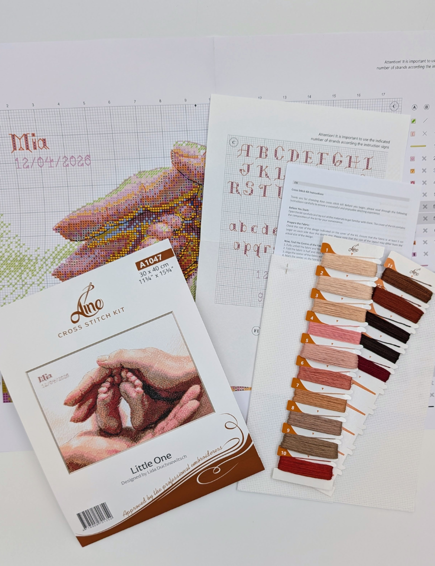 The A1047 Little One cross-stitch kit box laid out with the colour chart, an alphabet chart, the instruction sheet, pre-sorted threads on numbered cards and white Aida fabric.