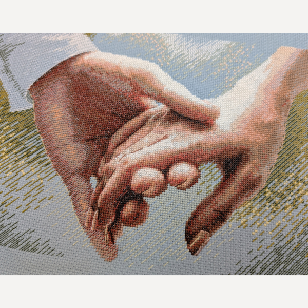 Close-up of the cross-stitched clasped hands on blue Aida, showing the blended peach, rose and brown thread shading and the fine outline backstitch on the fingers.