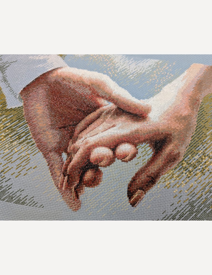 Close-up of the cross-stitched clasped hands on blue Aida, showing the blended peach, rose and brown thread shading and the fine outline backstitch on the fingers.