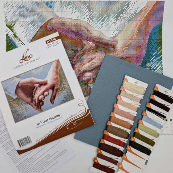 The A1046 In Your Hands cross-stitch kit box laid out with the colour chart, instruction sheet, blue Aida fabric and pre-sorted threads on numbered cards.