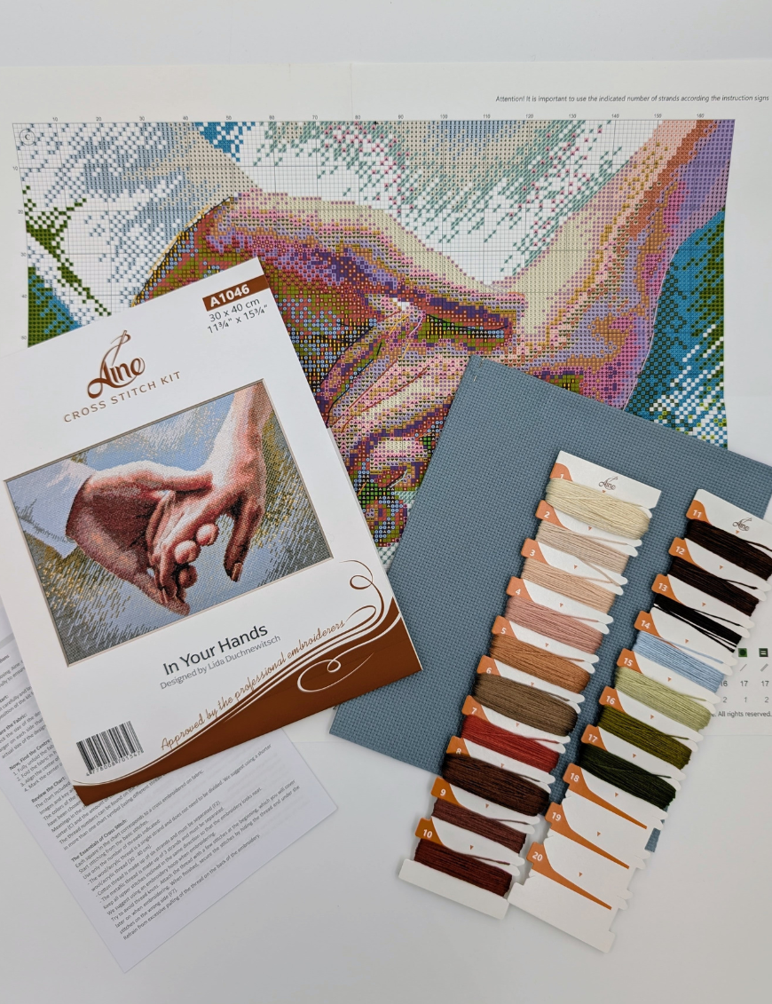 The A1046 In Your Hands cross-stitch kit box laid out with the colour chart, instruction sheet, blue Aida fabric and pre-sorted threads on numbered cards.