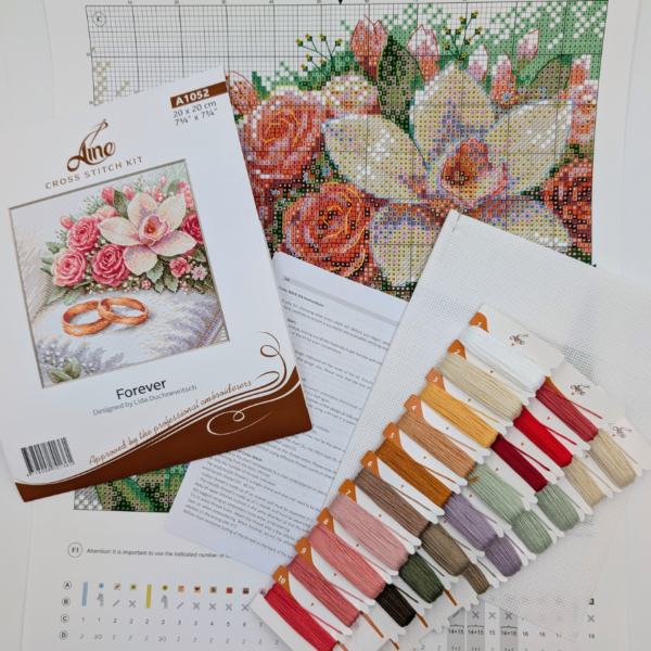 The A1052 Forever cross-stitch kit box laid out with the colour chart, instruction sheet, white Aida fabric and pre-sorted threads on numbered cards in pink, red, green, gold and purple shades.